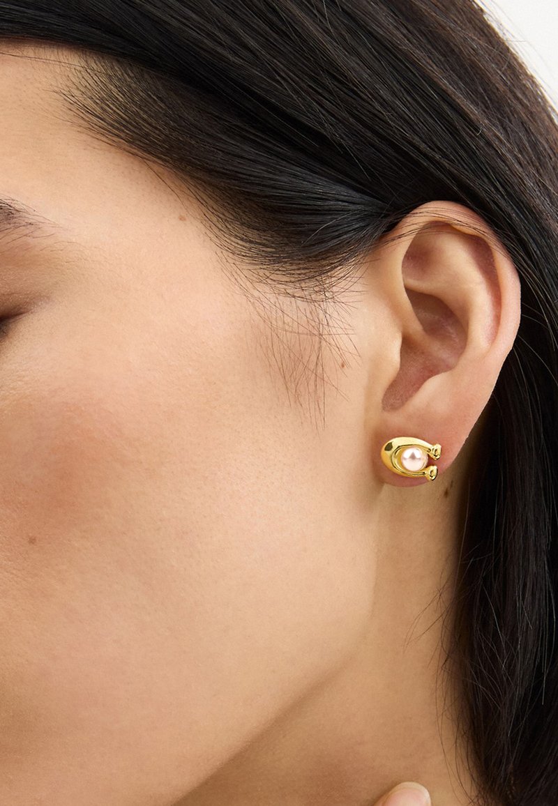Gold earrings featuring a round pearl set in a unique, structured design. Smooth texture with polished surfaces and secure backing.