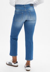 Blue denim jeans with a straight cut, mid-rise waist, five pockets, and contrasting stitching. Accompanied by white sneakers with black accents.