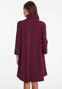 Robe bordeaux jusqu'aux genoux avec un col montant, des manches trois-quarts et une texture lisse. Présente une silhouette A-line ample.