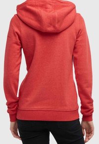 Rød hættetrøje med en børstet tekstur, ribbede manchetter og kant. Har en kengurulomme og syninger langs skuldrene.