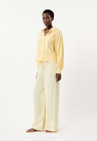 Chemise jaune clair à boutons avec poche et détails brodés, associée à un pantalon ample à rayures jaunes pâles. Coupe décontractée, texture douce.