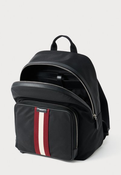 Black nylon backpack with a front pocket featuring a red and white stripe. Zipper closures and leather accents are present. Two top handles.
