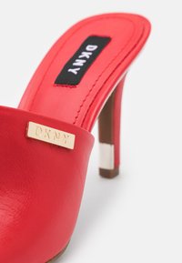 Mule à talons hauts en cuir rouge avec un plaquage doré du logo DKNY. Présente une texture lisse, un design ouvert et un talon effilé.