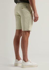 Shorts vert clair avec une coupe slim, poches avant et arrière, et une texture subtile. Portés avec des baskets blanches.