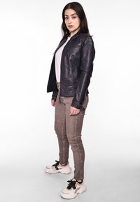 Schwarze Lederjacke mit Reißverschluss vorne, taillierter Passform und dekorativer Naht. Kombiniert mit beigen Slim-Fit-Hosen und weißen Sneakern.