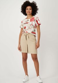 Shorts beige courts avec une taille nouée, associés à un t-shirt graphique multicolore présentant des palmiers et des voitures anciennes. Baskets blanches.