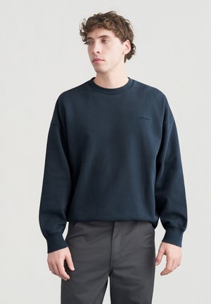 Granatowa bluza z mieszanki bawełny, z okrągłym dekoltem, ściągaczami na rękawach oraz subtelnym logo na piersi, zestawiona z szarymi spodniami.