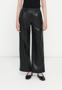Zwarte faux leren wijde broek met een gladde textuur, hoge taille, voorkanten en een subtiele glans. Gecombineerd met zwarte platte schoenen.