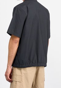 Kortärmad svart overshirt i bomull, med kragkrage och elastisk nederkant för en kroppsnära look.