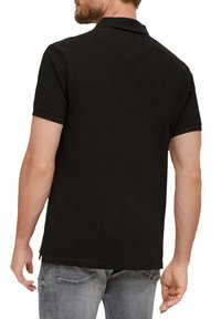 Zwarte polo met een klassieke kraag, korte mouwen en een gestructureerde stof. Heeft een rechte zoom en discrete zijsplitten.