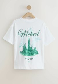 Valge puuvillane T-särk, millel on roheline graafika Smaragdlinna teemal, peal "Wicked" tekst ja kergelt tekstuurne print. Üksikasjalik lõige.
