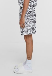 Black and white patterned shorts with a loose fit, made of lightweight fabric. Paired with white slides and ankle socks. Simple design.