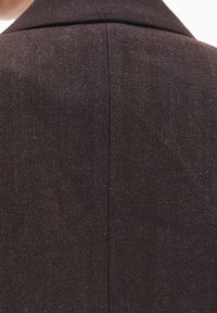 Tela de abrigo en espiga marrón con cuello entallado. Presenta un patrón texturizado y tejido, y una costura central en la parte posterior.