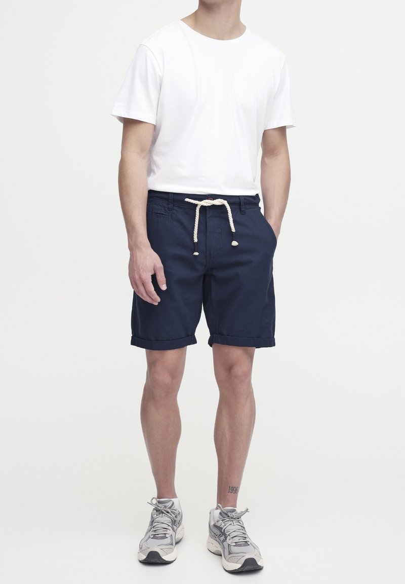 Shorts bleu marine avec taille à cordon, t-shirt en coton blanc et baskets grises ; les shorts ont des ourlets retroussés et des poches avant.