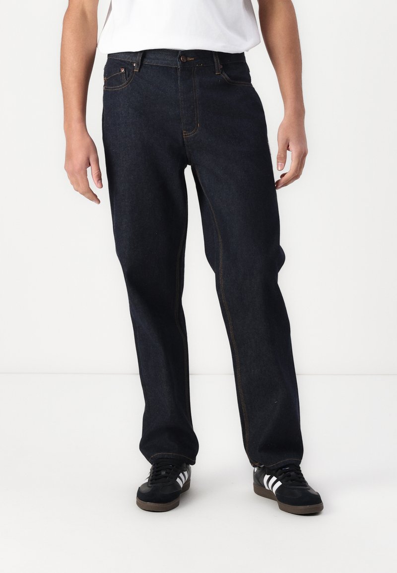 Dark blue denim jeans with straight-leg cut, visible orange stitching, and front and back pockets. Worn with black sneakers.