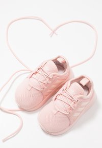 Rosa sportskor med meshuppbyggnad, snörning och en dämpad sula. Tre vita ränder på sidorna. Snören i form av ett hjärta.