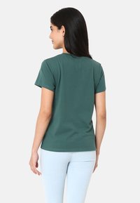 T-shirt en coton vert avec un col rond et des manches courtes, présenté de dos. Design simple, texture lisse, silhouette ajustée.