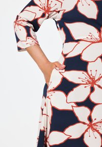 Abito floreale blu navy con grandi motivi di fiori bianchi e arancioni. Presenta maniche a tre quarti e tasche laterali. Tessuto morbido.