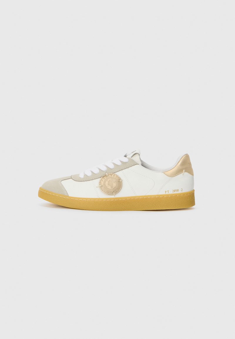 Hvit lær sneaker med beige detaljer, gummisåle, rundt logoelement på siden, flate snører og suède tåhette. Teksturerte overflater på materialene.