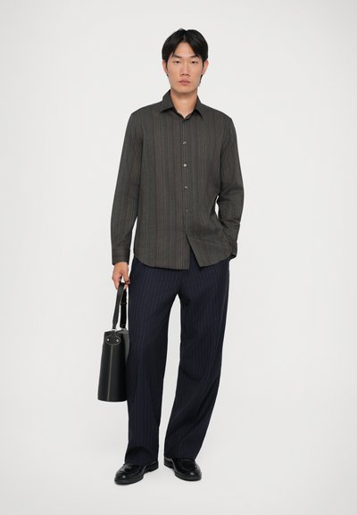 Camisa de manga larga a rayas en tonos oscuros con cuello, combinada con pantalones azul marino a rayas y una bolsa cilíndrica negra. Textura de tela suave.