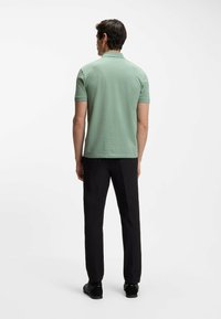 Camiseta tipo polo verde con un patrón texturizado, mangas cortas y cuello tipo canalé, combinada con pantalones negros y zapatos oscuros.