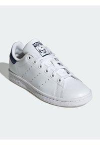 Sneaker Adidas Stan Smith bianchi con il tallone blu navy, strisce perforate ai lati e etichetta sulla linguetta con un ritratto.