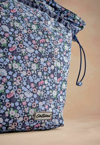 Sac à cordon floral en tissu bleu marine avec des fleurs roses, bleues et blanches ; il dispose d'une étiquette de marque et d'une finition texturée.