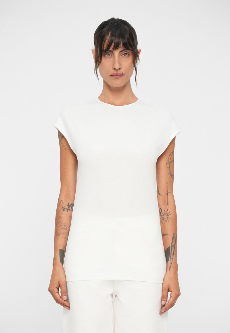 Haut blanc à manches courtes avec un col rond et une texture lisse, présentant un buste ajusté et un ourlet ample.