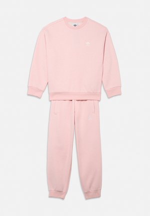 Vaaleanpunainen Adidas-collegepaita ja -collegehousut, joissa on ribbineulotut hihansuut sekä valkoiset kolmilapaiset logot rinnassa ja reisissä.