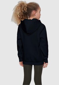 Svart hettegenser med lange ermer, ribbet mansjetter og nederkant. Båret over olivengrønne leggings, sett fra baksiden. Myk stofftekstur.