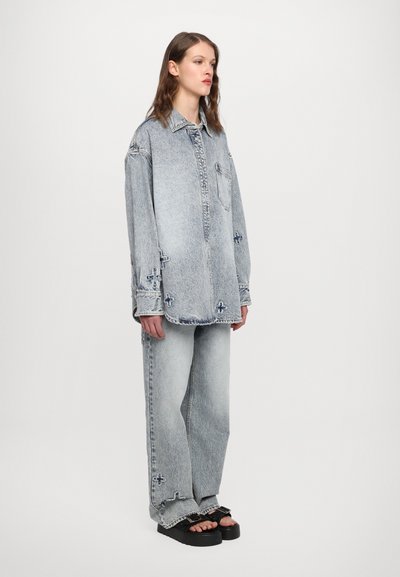 Šviesiai mėlynas džinsinis oversize marškinis su kišene ir siūlų akcentais. Pora su atitinkamais baggy džinsais ir masyviomis juodomis sandalais.