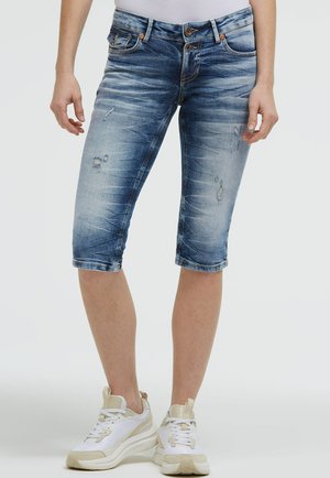 Person wearing faded blue distressed denim knee-length shorts and white sneakers with beige accents on a light background.