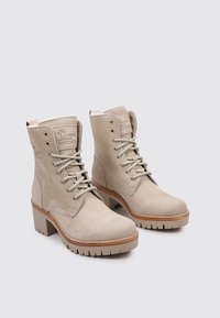 Beige Wildlederstiefeletten mit gepolstertem Kragen, Schnürung vorne und blockiertem Absatz. Strukturierte Oberfläche mit sichtbaren Nähten und Gummisohle.