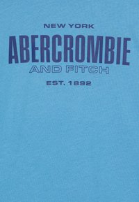 Niebieska bawełniana koszulka z ciemnoniebieskim napisem "NEW YORK ABERCROMBIE AND FITCH EST. 1892" w wyraźnej czcionce.