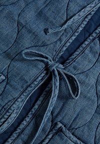 Jeansjacka med quiltat mönster, mörkblå färg och knytning i midjan. Inkluderar accenttrådar och ett lagerdesign.