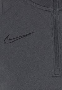 Gros plan sur un tissu gris foncé avec un logo Nike swoosh noir brodé et une fermeture éclair verticale sur le côté droit.