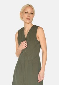 Ärmelloses olivgrünes Kleid aus leichtem Stoff, mit einem Reißverschluss vorne und dezenten Nähten für Textur.