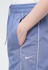 Svetlomodré športové šortky s elastickým pásom a sťahovacou šnúrkou, s bočnými vreckami a bielym lemovaním pozdĺž švov. Viditeľné logo Nike.