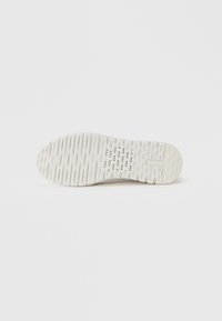 Semelle de basket blanche en caoutchouc texturé, présentant un motif de bande de roulement et de petits trous de ventilation. Bords lisses et absence de marquage visible.