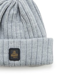 Berretto a maglia grigio con una superficie a coste e un risvolto piegato. Caratterizzato da una toppa quadrata nera con un logo dorato. Materiale morbido e caldo.