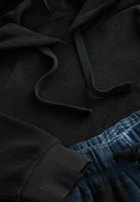 Čierna fleecová mikina s kapucňou a šnúrkami, doplnená modrými teplákmi so šnúrkami a textúrovaným pásom.