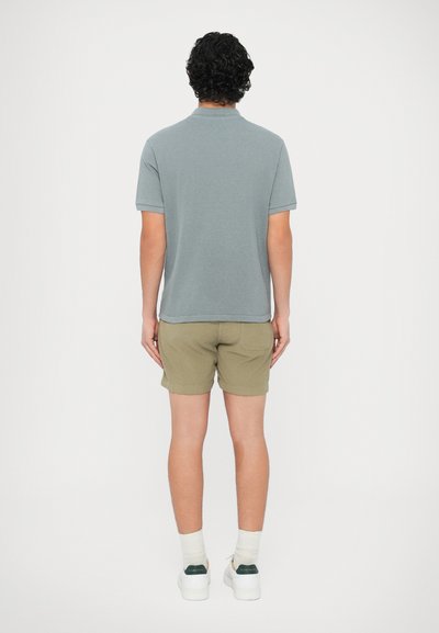 Γκρι κοντομάνικο πόλο μπλουζάκι συνδυασμένο με χακί πράσινο σορτς. Το σύνολο έχει χαλαρή εφαρμογή, απαλό ύφασμα και απλό σχεδιασμό.
