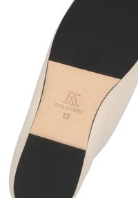 Suola di scarpa beige con punta e tacco neri, impressa con il logo del marchio, la scritta "PELLE VERA" e la taglia "37" sulla sezione in pelle.