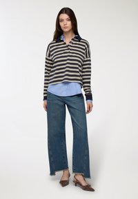 Camicia a righe con colletto in blu navy, crema e beige, abbinata a una camicia azzurra. Jeans a gamba larga con orli grezzi e mule con tacco marroni.