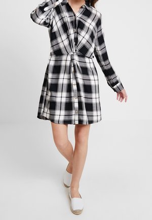 Schwarz-weiß kariertes Hemdkleid mit Knopfleiste, langen Ärmeln und Frontknotendetail; aus gewebtem Stoff mit weicher Textur.