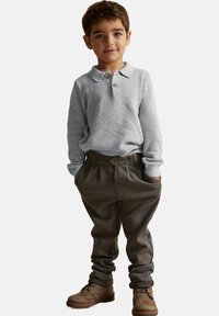 Ljust grått texturerat långärmat polo skjorta med krage och knapp, i kombination med bruna löstsittande byxor och bruna stövlar.