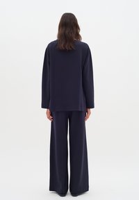 Námořnická modrá, oversized top s dlouhými rukávy, spárovaný s širokými kalhotami ve stejném odstínu. Měkká látka, minimální šití a uvolněný střih.