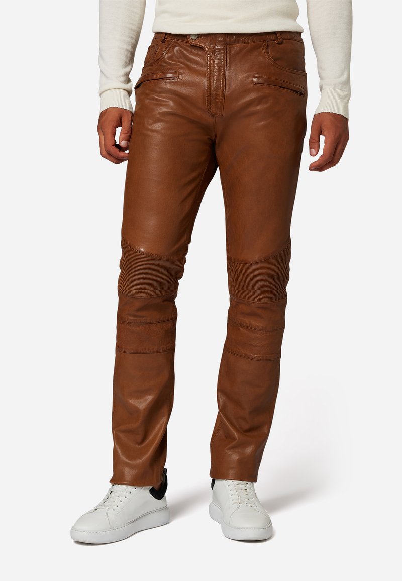 Bruine leren broeken met een slim fit ontwerp, uitgerust met geribbelde accenten op de knieën en ritszakken. Gedragen met witte sneakers.