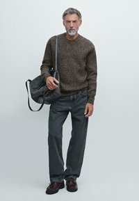 Brązowy sweter robiony na drutach, szare dżinsy, ciemne skórzane buty, czarna skórzana torba na ramię, teksturowana tkanina, luźny krój.