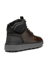 Zapato de cuero marrón de media altura con acentos de textil negro, suela de goma y cuello acolchado. Presenta ojales reforzados y superficie texturizada.